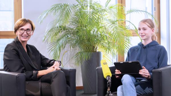 Kinderreporter Kjell interviewt Bildungsministerin Bettina Stark-Watzinger, zwischen den beiden steht ein "Team Timster"-Mikrofon